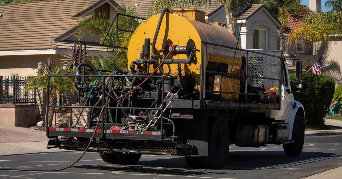 A close-up of a pick-up truck with a sealcoat machine on the vehicle's bed. The machine is in use.