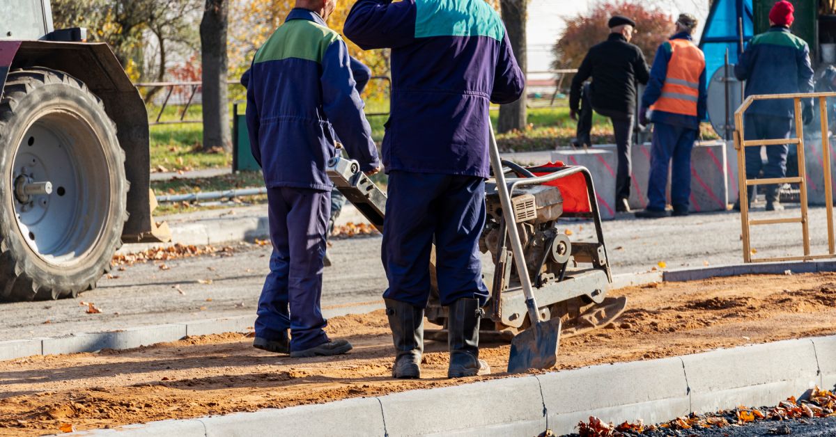 A worker compresses sand for paving slabs with a special working tool to help repair asphalt pavement.