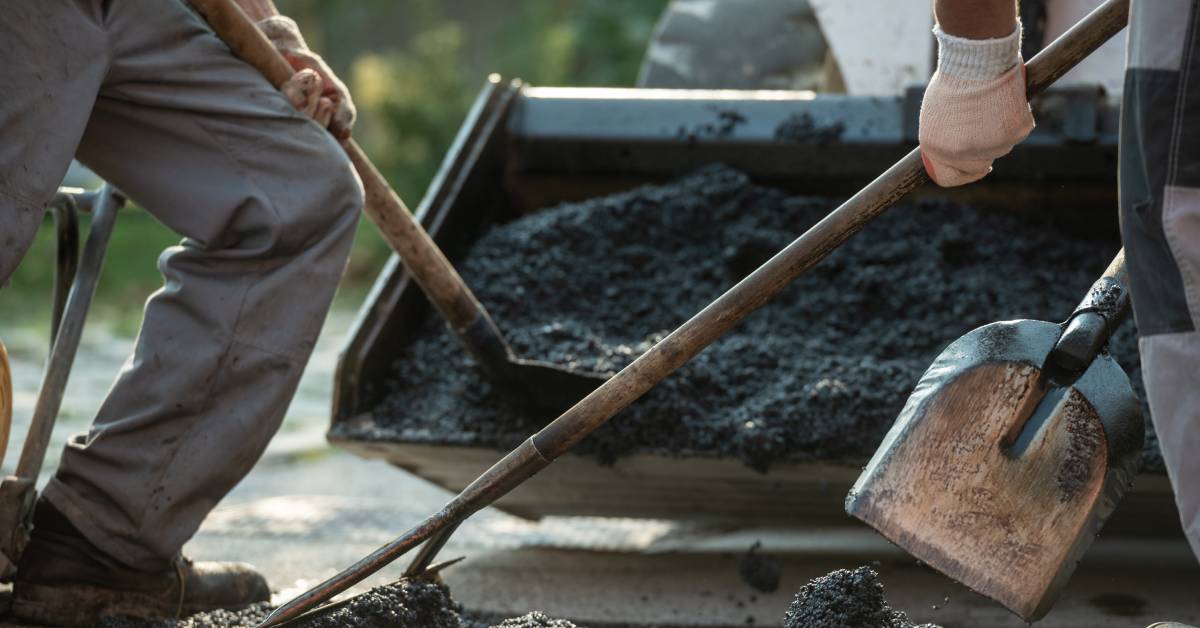 A close-up of three workers' shovels raking and tamping the ground as they pour more asphalt.