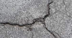 A close-up of a cracked and damaged asphalt parking lot, road, or driveway that needs to be repaired.