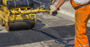 A close-up of a worker installing an asphalt speed bump. They're wearing safety gear and using an asphalt machine.