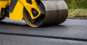 An asphalt road roller with a heavy vibration roller compactor pressing fresh asphalt onto a roadway on a construction site.