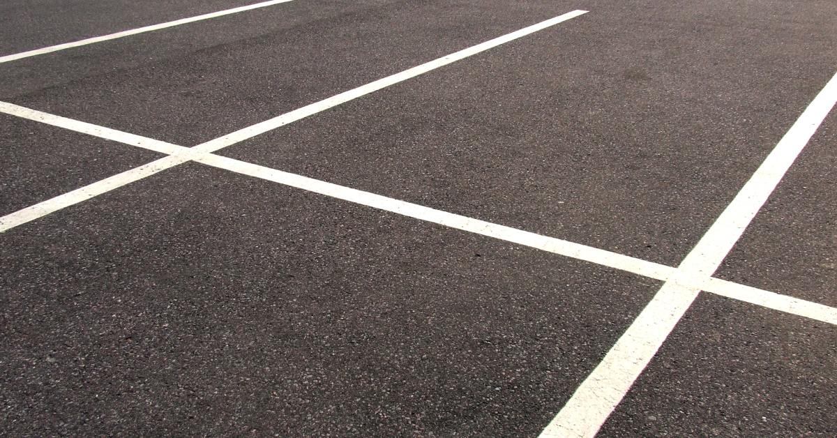 A vacant asphalt parking lot with clearly visible space lines, mostly clean but with some areas showing wear.