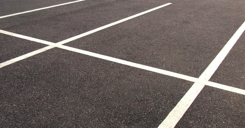 A vacant asphalt parking lot with clearly visible space lines, mostly clean but with some areas showing wear.