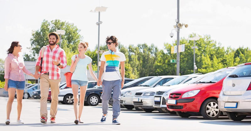 A group of four people—two men and two women—chatting as they walk side by side through a parking lot.