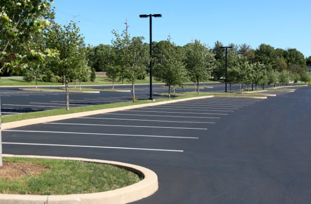 A parking lot with fresh striping for the parking spaces surrounded by small trees and neatly mowed grass.