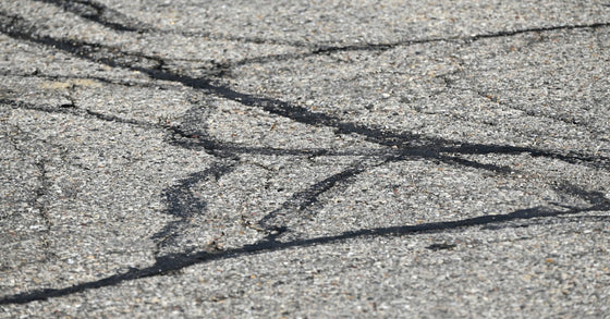 A close view of black sealant filling narrow cracks in a gray asphalt surface during pavement repair work.