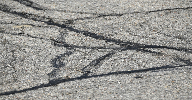 A close view of black sealant filling narrow cracks in a gray asphalt surface during pavement repair work.