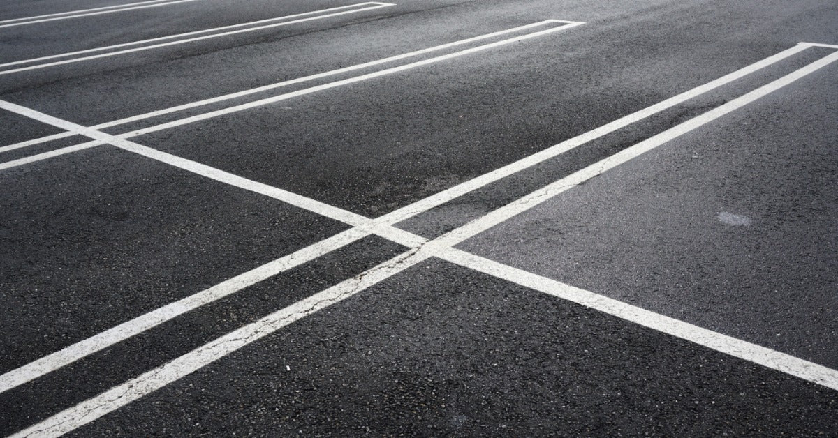 A cracked asphalt parking lot with faded painted striping across the surface showing wear and uneven texture.
