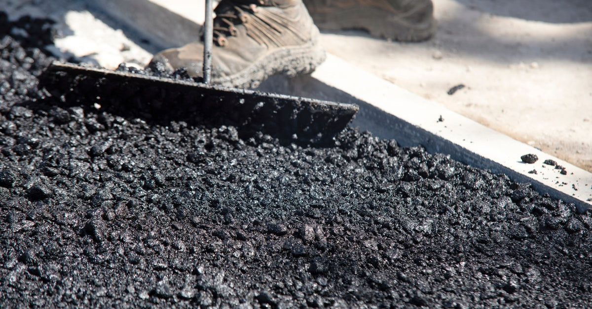 A group of workers spreading and leveling fresh black asphalt using tools and paving equipment at a construction site.