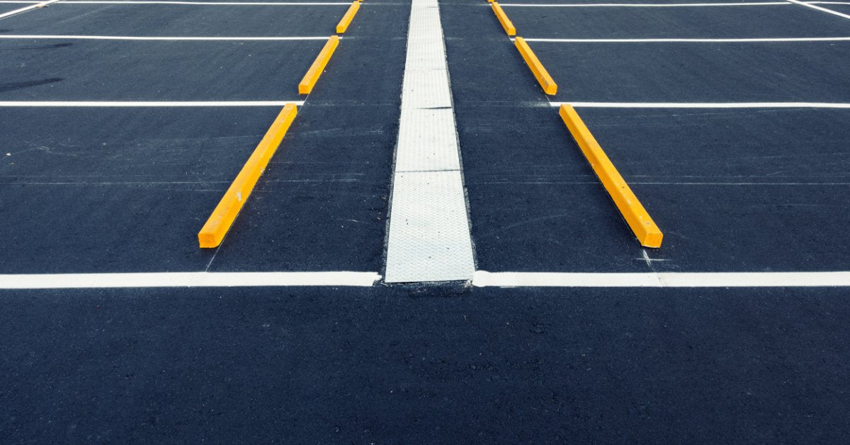 An empty asphalt parking lot with white painted spaces, yellow wheel stops, curbs, and pavement markings.