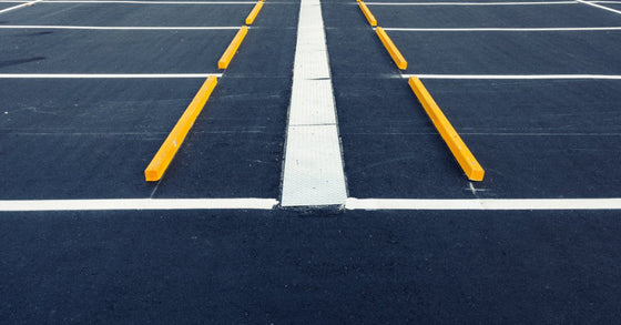 An empty asphalt parking lot with white painted spaces, yellow wheel stops, curbs, and pavement markings.