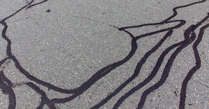 Grey asphalt pavement has a yellow stripe and a lot of black lines showing where cracks have previously been filled.