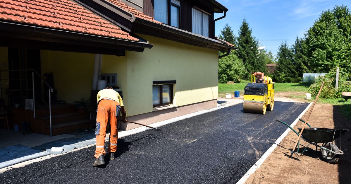 Two large yellow road roller machines drive over thick fresh black asphalt pavement during the daytime.
